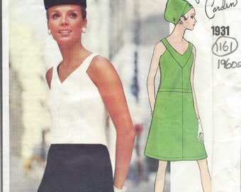 May include: A vintage sewing pattern featuring two dress designs by Pierre Cardin. The pattern is from 1961 and includes a white sleeveless dress with a black skirt and a green sleeveless dress. The model wearing the white dress is also wearing a black hat.