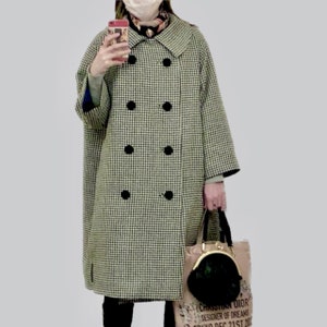 May include: A black and white checked coat with a double breasted closure and black buttons. The coat has a collar and is worn over a patterned scarf. The person is holding a brown bag with a black purse.