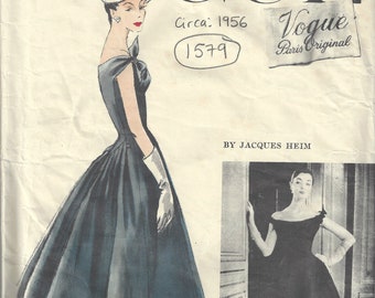 May include: A vintage Vogue Paris Original pattern for a dress by Jacques Heim, circa 1956. The pattern number is 1579. The illustration shows a woman wearing a black dress with a full skirt and a white hat.