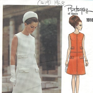 May include: A vintage Vogue Couturier Design pattern from 1968. The image features a woman in a white sleeveless dress with pockets, a matching hat, and gloves. A fashion illustration shows an orange dress with pockets.