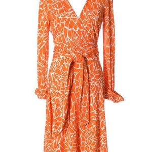 May include: A long-sleeved orange wrap dress with a white abstract floral print. The dress has a V-neckline, a self-tie belt, and long sleeves with buttoned cuffs.