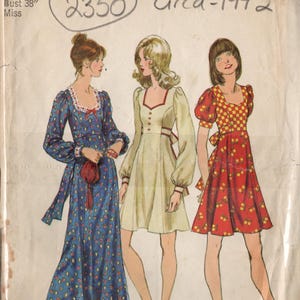 Może przedstawiać: Wzorzec szycia vintage Simplicity numer 5347 na sukienkę, około 1972 roku. Wzorzec zawiera trzy różne style sukienek, jedną w kolorze niebieskim w białe kropki, jedną w kolorze białym z czerwoną lamówką i jedną w kolorze czerwonym w żółto-białą kratę. Wzorzec jest dla rozmiaru 16, obwód biustu 96,5 cm.