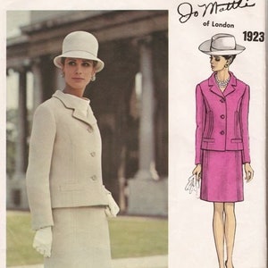 May include: A vintage sewing pattern for a two-piece suit with a jacket and skirt. The pattern is for a white suit with a pink skirt and features a white hat. The pattern is from Vogue Couturier Design, Jo Matte of London, 1923.