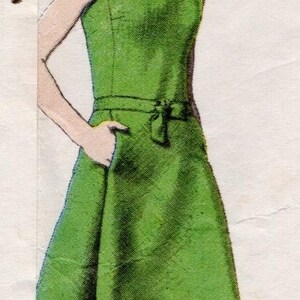 Könnte beinhalten: Ein ärmelloses, knielanges grünes Kleid mit rundem Ausschnitt, körperbetontem Oberteil und einer Taille, die mit einem schmalen Gürtel akzentuiert ist. Der Rock hat eine ausgestellte Silhouette und seitliche Taschen. Die Abbildung zeigt eine Kopfbedeckung.