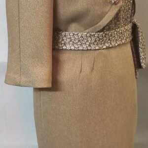 May include: A brown dress suit with a matching jacket and skirt. The jacket has three-quarter sleeves and a brown and white patterned belt. The skirt is knee-length.