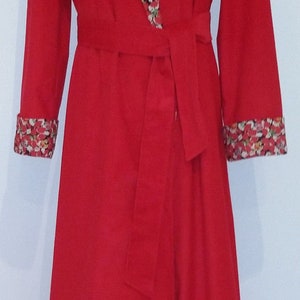 May include: A long, red robe with a floral print collar and cuffs. The robe has a matching belt and is displayed on a mannequin. The floral pattern includes red, white, and yellow flowers.