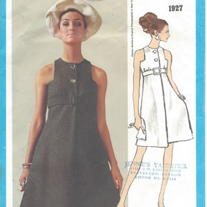 May include: A vintage sewing pattern for a sleeveless dress with a button-up front and a belt. The pattern is from Vogue Americana and is for size 19605, style number R573. The pattern is for a dress with a simple, classic design.