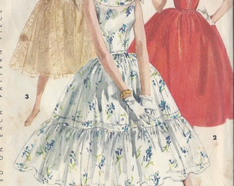 May include: Vintage sewing pattern for a dress with a full skirt. The pattern is from 1955 and is size 14. The dress has a scoop neck and a fitted bodice. The skirt is full and has a gathered ruffle at the hem. The pattern includes instructions for making the dress.