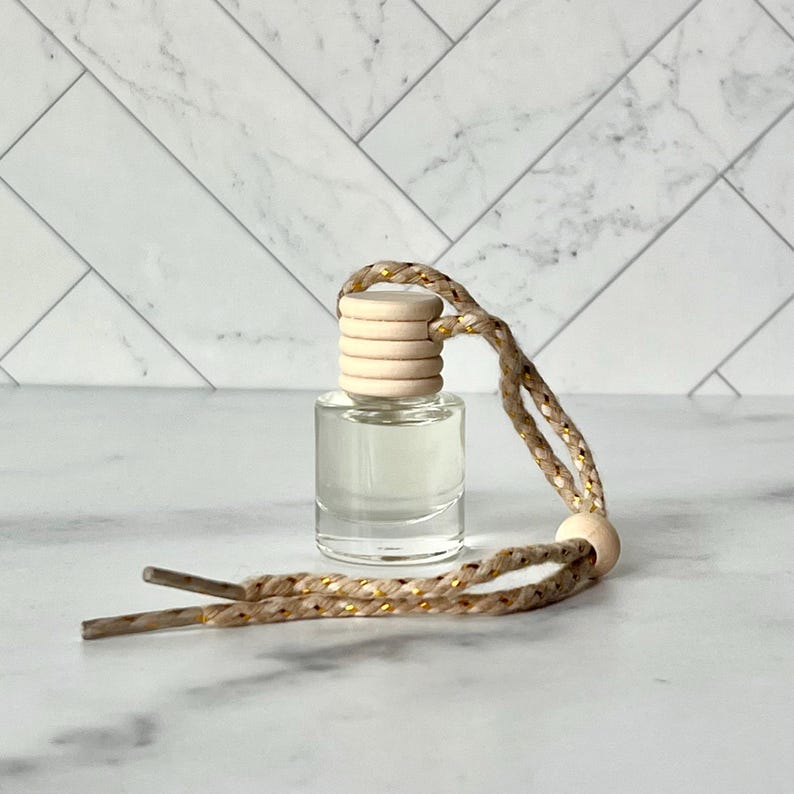 以下が含まれることがあります： 木製のキャップと装飾的なロープが付いた、小さな透明なガラス瓶。ロープは金色のアクセントが付いたタン色で、木製のビーズに取り付けられています。ボトルには透明な液体が入っています。おそらく芳香剤または香りのディフューザーです。