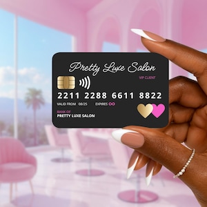 Pode incluir: Um cartão VIP preto Pretty Luxe Salon com ícones de coração dourados e rosa. O cartão exibe o nome do salão, o número da conta e a data de validade. O cartão é segurado em frente a um fundo de salão rosa desfocado.