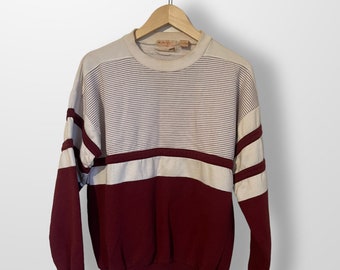 May include: A striped white and burgundy sweatshirt with a crew neck. The sweatshirt has a white stripe across the chest and two white stripes on each sleeve.