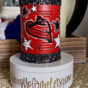 May include: A cylindrical red metal container featuring black and white star illustrations and a central heart design. The top and bottom rims are decorated with black glitter. The container rests on a white circular base with the text KickingUpGravel.etsy.com.