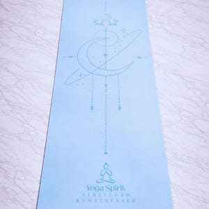 Pu&ograve; includere: Un tappetino da yoga azzurro con un design celeste e le parole "Yoga Spirit, Stretched & Unstressed." Il tappetino presenta una luna crescente, stelle e una figura seduta. Ideale per yoga e meditazione.
