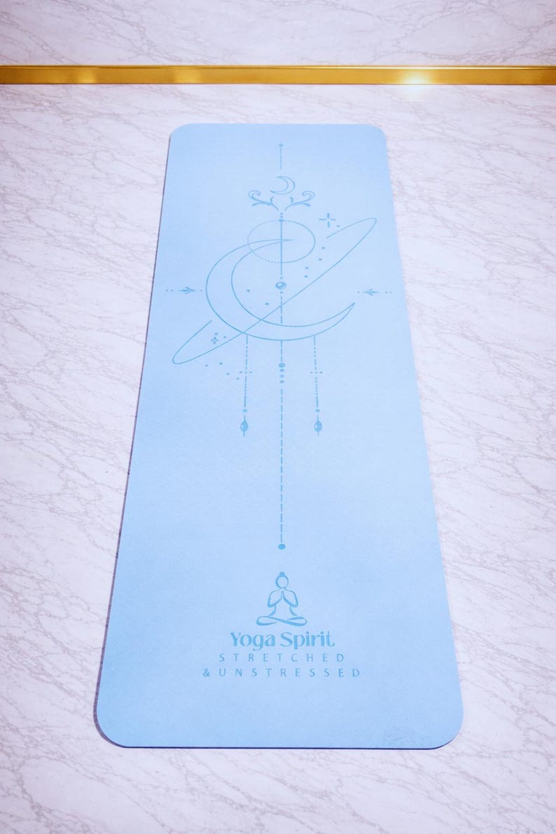 Pu&ograve; includere: Un tappetino da yoga azzurro con un design celeste e le parole "Yoga Spirit, Stretched & Unstressed." Il tappetino presenta una luna crescente, stelle e una figura seduta. Ideale per yoga e meditazione.