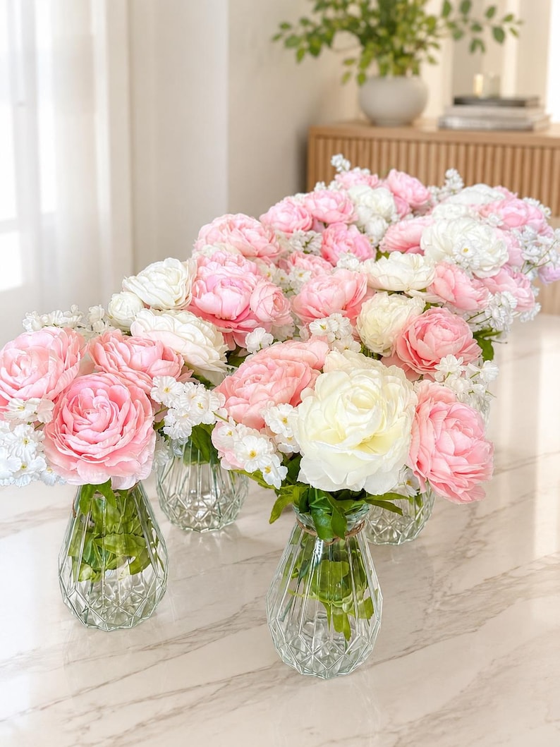 May include: A collection of clear, diamond-patterned glass vases, each filled with a lush arrangement of soft pink and white peony-like flowers and small white filler blossoms, featuring green stems visible through the transparent glass.