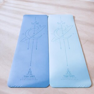 Pu&ograve; includere: Due tappetini da yoga blu con un design celeste. Ogni tappetino presenta una luna crescente, stelle e una figura seduta. I tappetini hanno il testo "Yoga Spirit Stretched Unstressed" in basso.