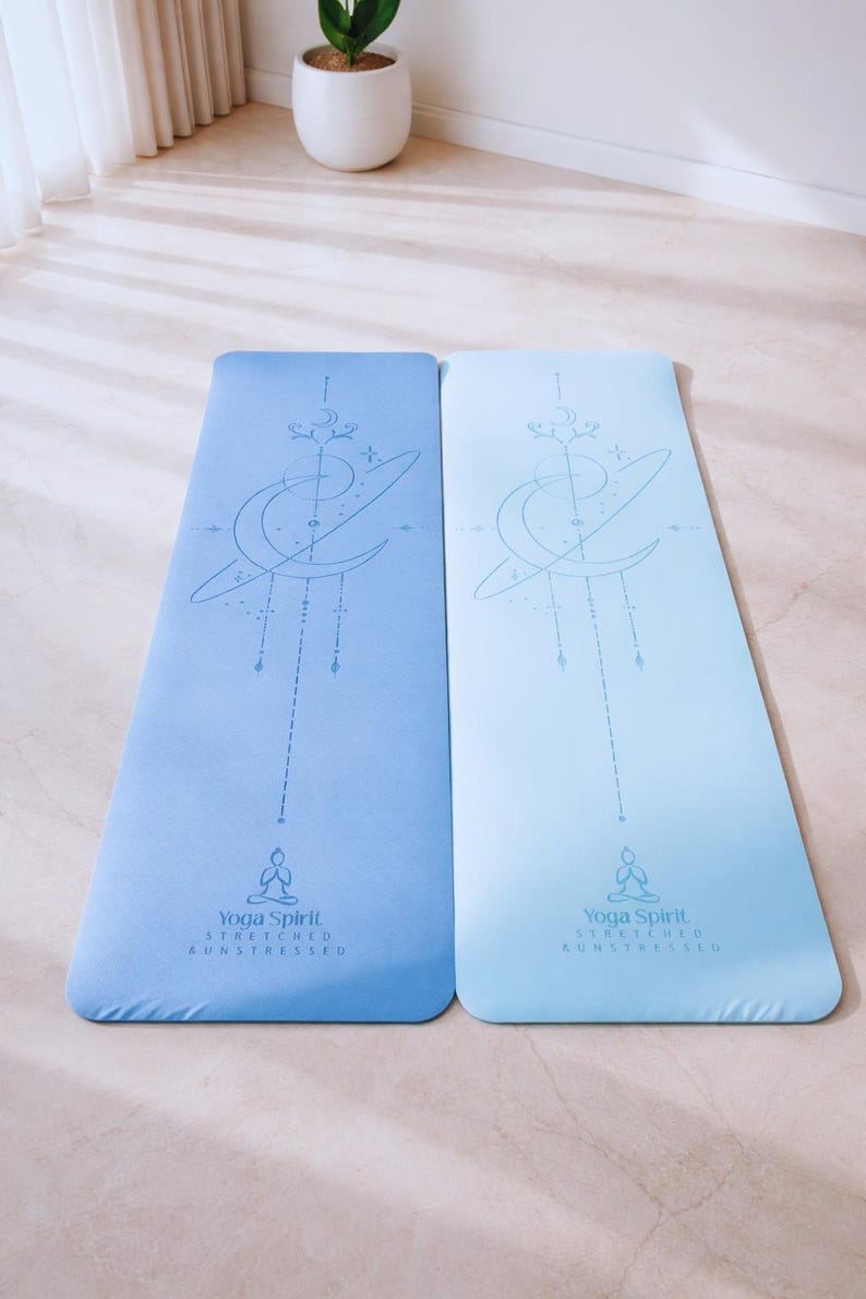 Pu&ograve; includere: Due tappetini da yoga blu con un design celeste. Ogni tappetino presenta una luna crescente, stelle e una figura seduta. I tappetini hanno il testo "Yoga Spirit Stretched Unstressed" in basso.