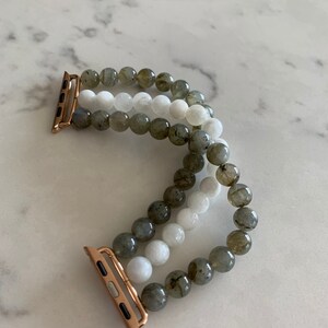 K&ouml;nnte beinhalten: Ein dreireihiges Armband f&uuml;r die Apple Watch mit grauen und wei&szlig;en Perlen. Das Armband hat einen ros&eacute;goldenen Verschluss.