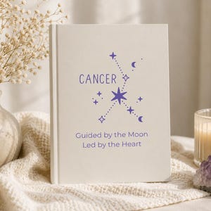 May include: A white hardcover book featuring the purple text CANCER, a constellation graphic, and the phrase Guided by the Moon Led by the Heart. The cover design includes small star and crescent moon icons arranged around the central star.