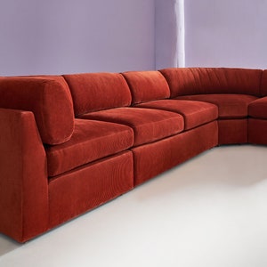 May include: A large, red sectional sofa with a modular design. The sofa has a deep, plush seat and a high back. The sofa is made of a soft, textured fabric.