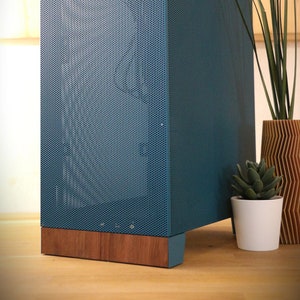 Puede incluir: Un altavoz azul con una rejilla de metal y una base de madera. El altavoz está sobre una superficie de madera.