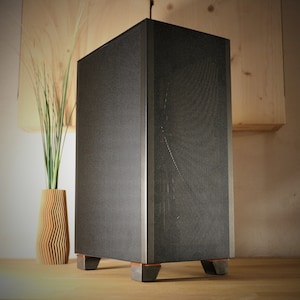 Op de afbeelding: Een zwarte computerbehuizing met een mesh-voorpaneel en een metalen zijpaneel. De behuizing heeft vier poten en staat op een houten oppervlak.