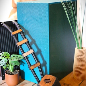Può includere: Un altoparlante turchese con una griglia in rete nera e una cornice in legno. L'altoparlante è appoggiato su un tavolo in legno con una piccola pianta in vaso e un vaso in legno con erba verde.
