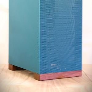 Puede incluir: Un mueble rectangular turquesa y azul con un panel frontal perforado. El mueble descansa sobre una base de madera. El diseño del mueble presenta una estética moderna, adecuada para uso doméstico o de oficina.