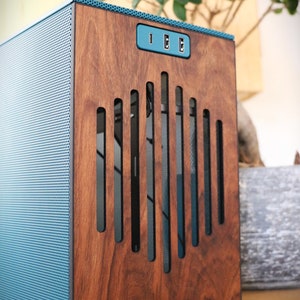 Peut inclure: Un haut-parleur bleu sarcelle et bois de noyer avec une grille métallique et un petit panneau avec trois boutons étiquetés "I", "D" et "E".