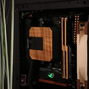 Può includere: Un case per computer con un dissipatore CPU in legno e una ventola beige. Il case è nero con un pannello frontale in mesh.