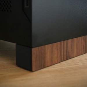 May include: A black computer case with a wooden base. The base is made of dark wood with a grain pattern.
