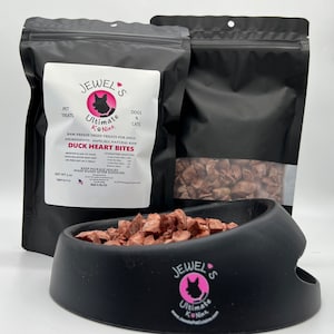 Puede incluir: Una bolsa negra resellable de golosinas para perros deshidratadas Jewel's Ultimate K-Nine de coraz&oacute;n de pato. La bolsa est&aacute; etiquetada con el nombre del producto, los ingredientes y el peso neto de 3 oz. Las golosinas tambi&eacute;n se muestran en un taz&oacute;n negro.