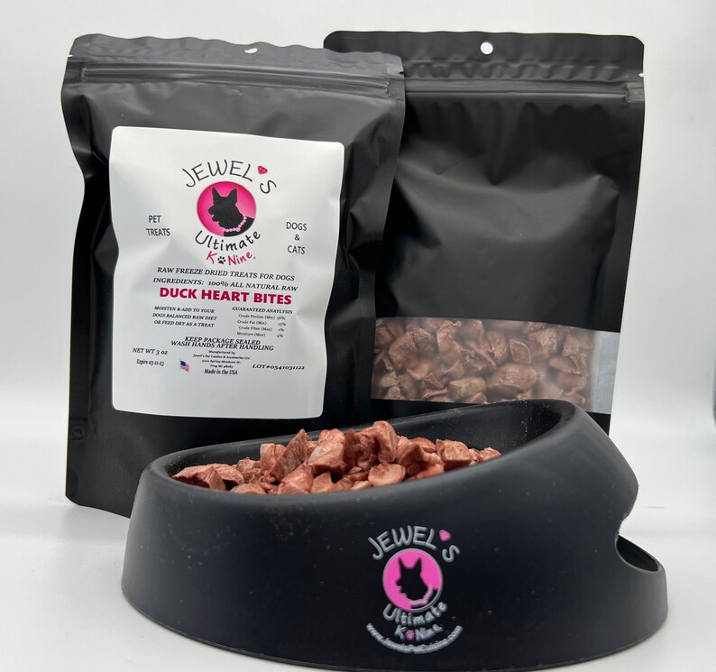 Puede incluir: Una bolsa negra resellable de golosinas para perros deshidratadas Jewel's Ultimate K-Nine de coraz&oacute;n de pato. La bolsa est&aacute; etiquetada con el nombre del producto, los ingredientes y el peso neto de 3 oz. Las golosinas tambi&eacute;n se muestran en un taz&oacute;n negro.