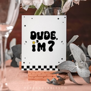 May include: White card with black text that says "Dude, I'm 7" with a yellow star and a lightning bolt. The card is on a wooden stand with a black and white chequered pattern at the bottom.