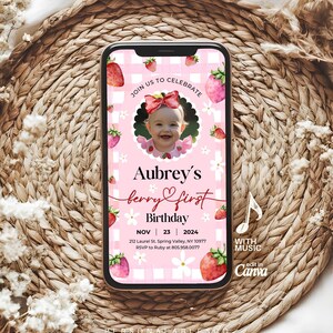 Op de afbeelding: Een digitale verjaardagsuitnodiging op een smartphonescherm met een roze en witte gingham achtergrond en aardbei-illustraties. De tekst luidt: JOIN US TO CELEBRATE, Aubrey's berry first Birthday, NOV 23 2024, 212 Laurel St. Spring Valley, NY 10977, RSVP to Ruby at 805.958.0077.
