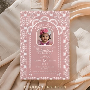 May include: A rectangular birthday invitation card in dusty rose with white lace-style borders. It features a central arched frame containing a photograph of a child wearing a floral crown, with text reading Cielito Lindo, Valentina's 1st Birthday, January 18, 2026, at 3 PM, 22 Devon St. Chatsworth, GA 30705, and RSVP to Raven at 975.665.6740.