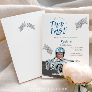 May include: A two-sided invitation with a racing theme. The front features a baby in a blue race car, the text "Growing Up Two Fast", and event details. The back is a blank white card with checkered flags.