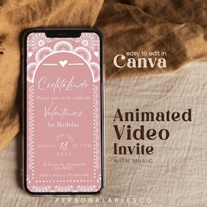 May include: A smartphone displays a pink digital invitation for a first birthday party. The invitation features the text "Cielito Lindo" and "Valentina's 1st Birthday." Additional text includes date, time, and RSVP information. The phone is on a tan surface.