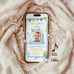 May include: A smartphone displaying a digital first birthday invitation for Adam, featuring a photo of a smiling baby, blue and yellow party bunting, balloons, and text details including the date, time, location, and RSVP information.