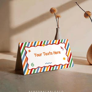 May include: A tent-style sign featuring a vibrant diagonal striped pattern in red, orange, yellow, green, and blue. The center displays a white scalloped-edge rectangle with the orange text Your Texts Here and small colorful graphic accents.