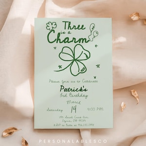 以下が含まれることがあります： 「Three is a Charm」の文字とクローバーのデザインが施された、薄緑色の招待状。3月14日午後5時からのパトリックの3歳の誕生日パーティーの招待状です。 RSVP情報が含まれています。