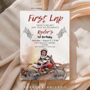 Puede incluir: Una tarjeta de invitación de cumpleaños rectangular con el texto First Lap, Ryder's 1st Birthday y detalles del evento. El diseño incluye dos banderas a cuadros, un niño con equipo de carreras en una moto roja y blanca y nubes de polvo.