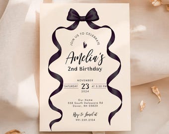 Puede incluir: Una tarjeta de invitación de cumpleaños color crema con un lazo negro en la parte superior y dos cintas largas y fluidas que enmarcan el texto. La tarjeta dice: Join us to celebrate Amelia's 2nd Birthday, Saturday November 23 2024 at 5:30 PM, 558 South Delaware Rd, Dover, NH 03820.