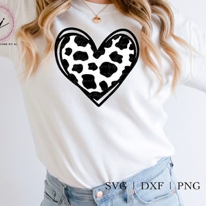 May include: A white t-shirt with a black and white cow print heart design. The text "SVG | DXF | PNG | EPS" is printed at the bottom of the shirt.