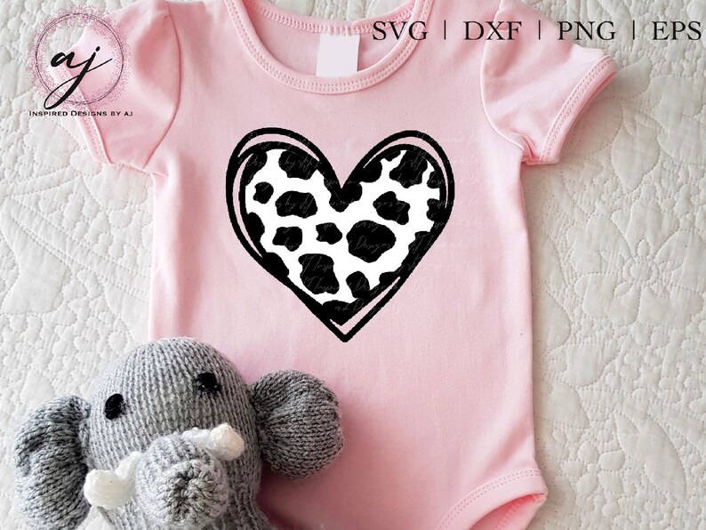 May include: A pink baby onesie with a black and white cow print heart design. The onesie is on a white surface with a gray stuffed elephant.