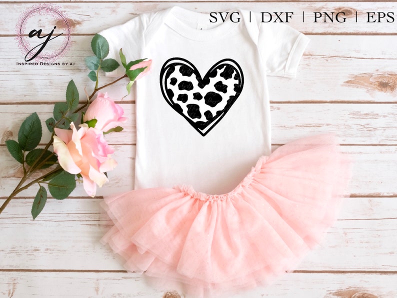 May include: A white onesie with a black and white cow print heart design. The onesie is paired with a pink tulle tutu.
