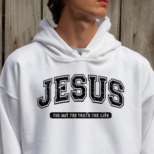 Op de afbeelding: Witte hoodie met het woord "JESUS" in een zwarte, versleten, collegiale lettertype. Daaronder staat de tekst "THE WAY THE TRUTH THE LIFE" in het zwart. De hoodie heeft een capuchon met trekkoord.