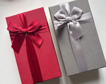 May include: Two rectangular gift boxes, one red and one gray, are displayed. Each box is adorned with a satin ribbon and bow. The red box has a matching red ribbon, while the gray box features a silver ribbon.