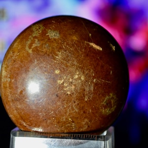 May include: A smooth, round, brown sphere with gold flecks and scratches. The sphere is sitting on a silver stand.