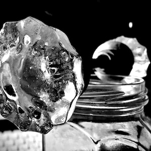 May include: A clear glass doorknob with a faceted design. The doorknob is attached to a glass jar with a metal lid.